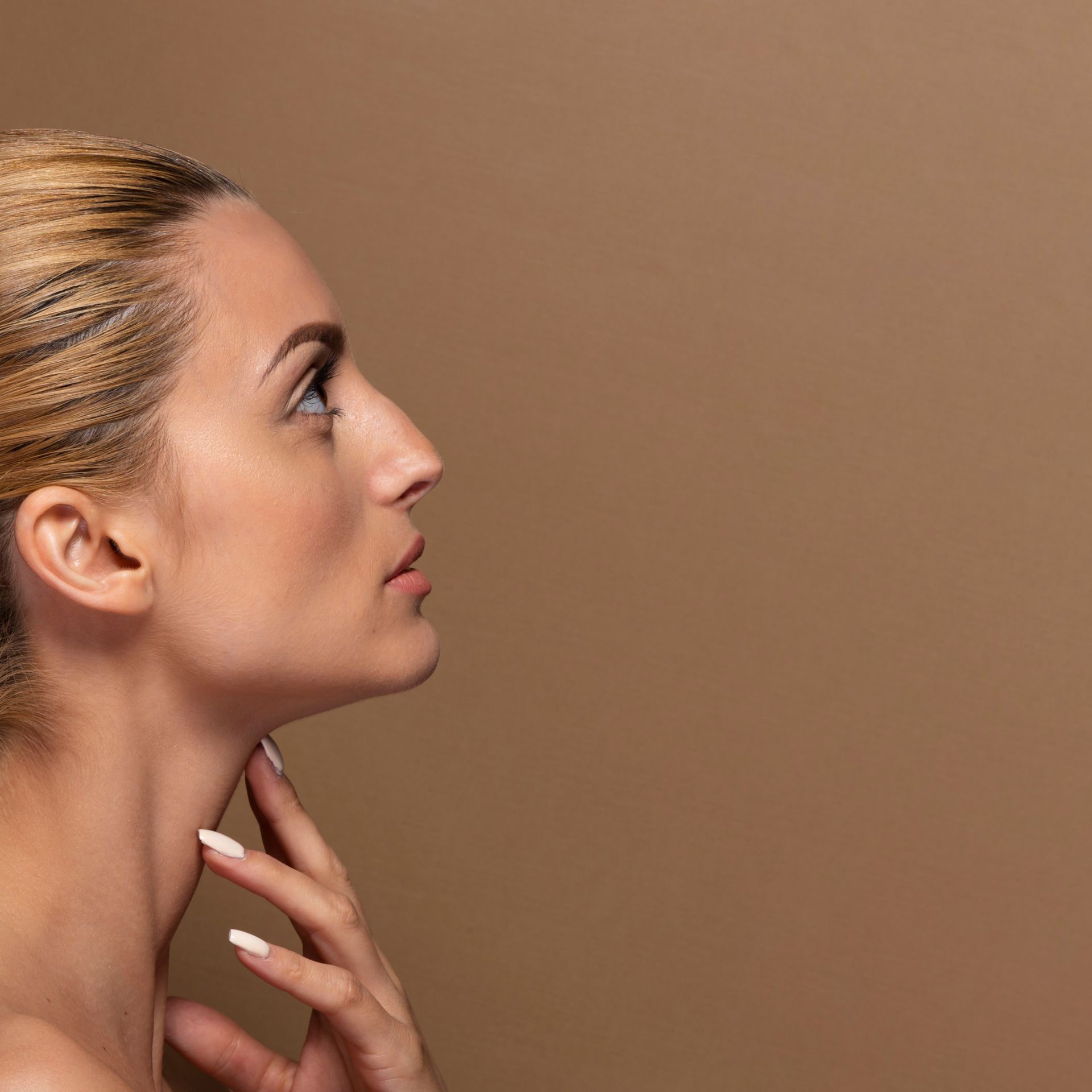 A close up of a woman 's face with her hand on her neck against a brown background.