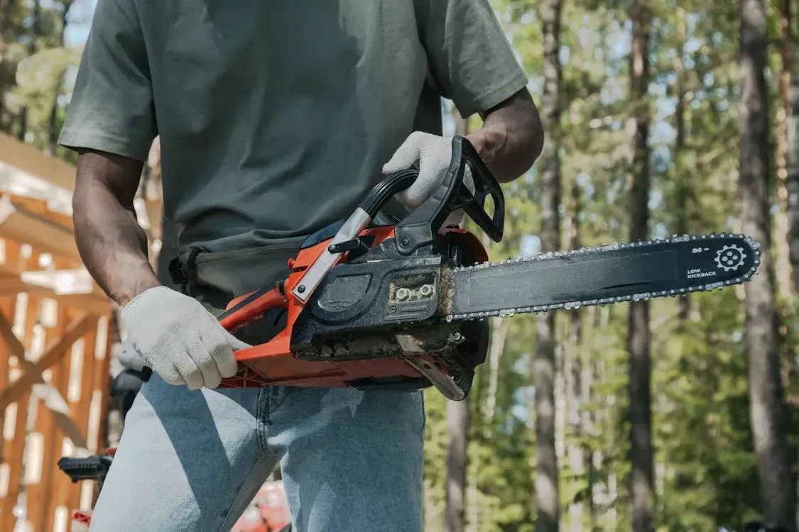 A man is holding a chainsaw in his hands in the woods.