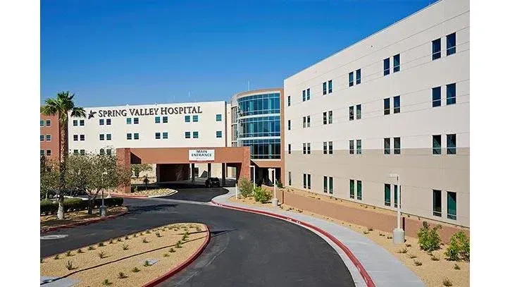 Modern hospital building with curved driveway and landscaped entrance under a clear blue sky