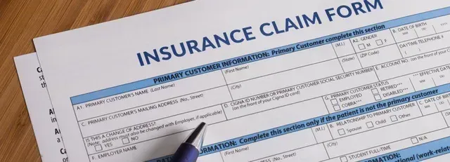 Insurance claim form on a desk with a pen, showing blue header text and handwritten entries.