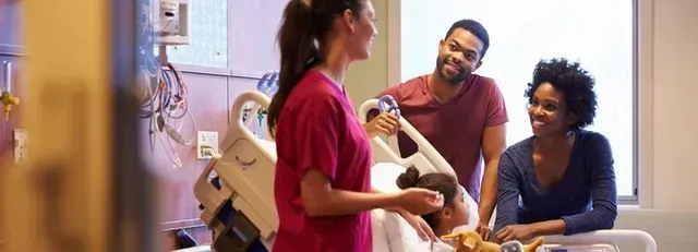 Three people chatting in a hospital room, with one person seated and another standing near a bed
