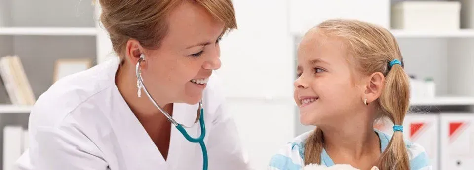 Doctor smiling and listening to a young girl with a stethoscope in a bright clinic