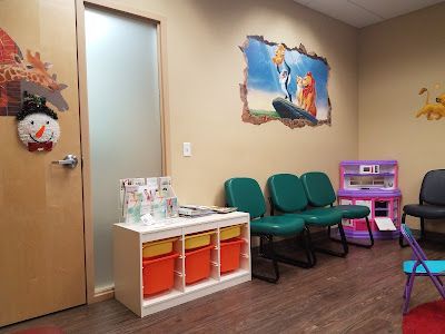 Waiting room with green chairs, toy shelf, and wall mural in a clinic or child care office.