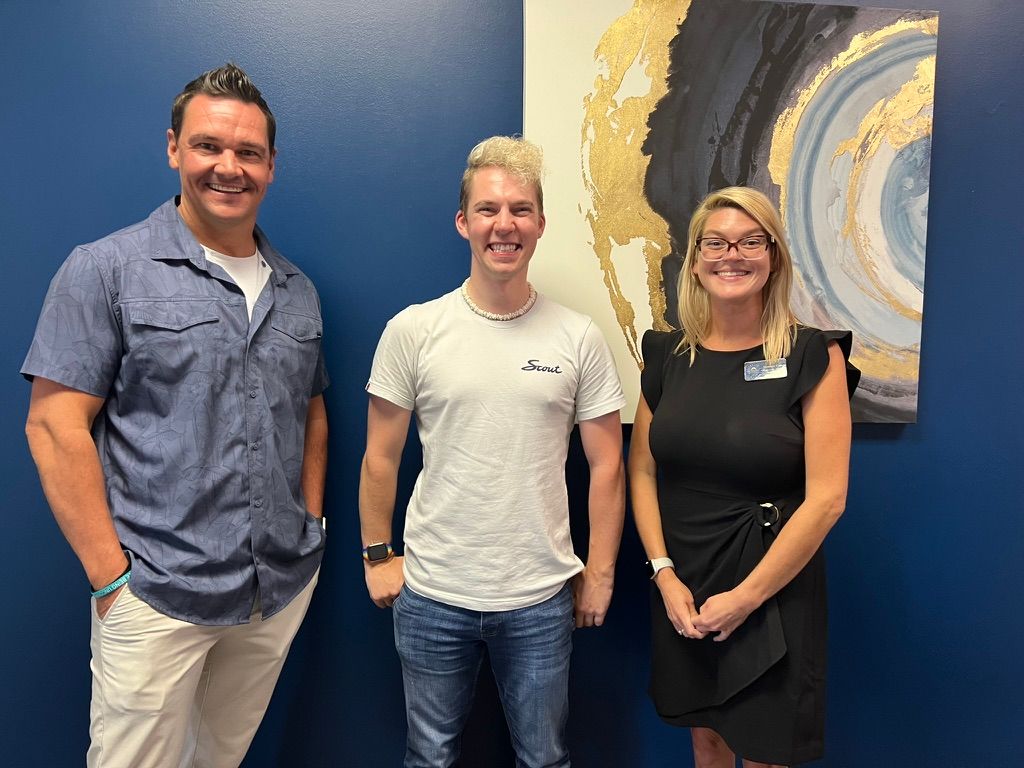 Three people standing and smiling in front of a large abstract painting in a gallery.