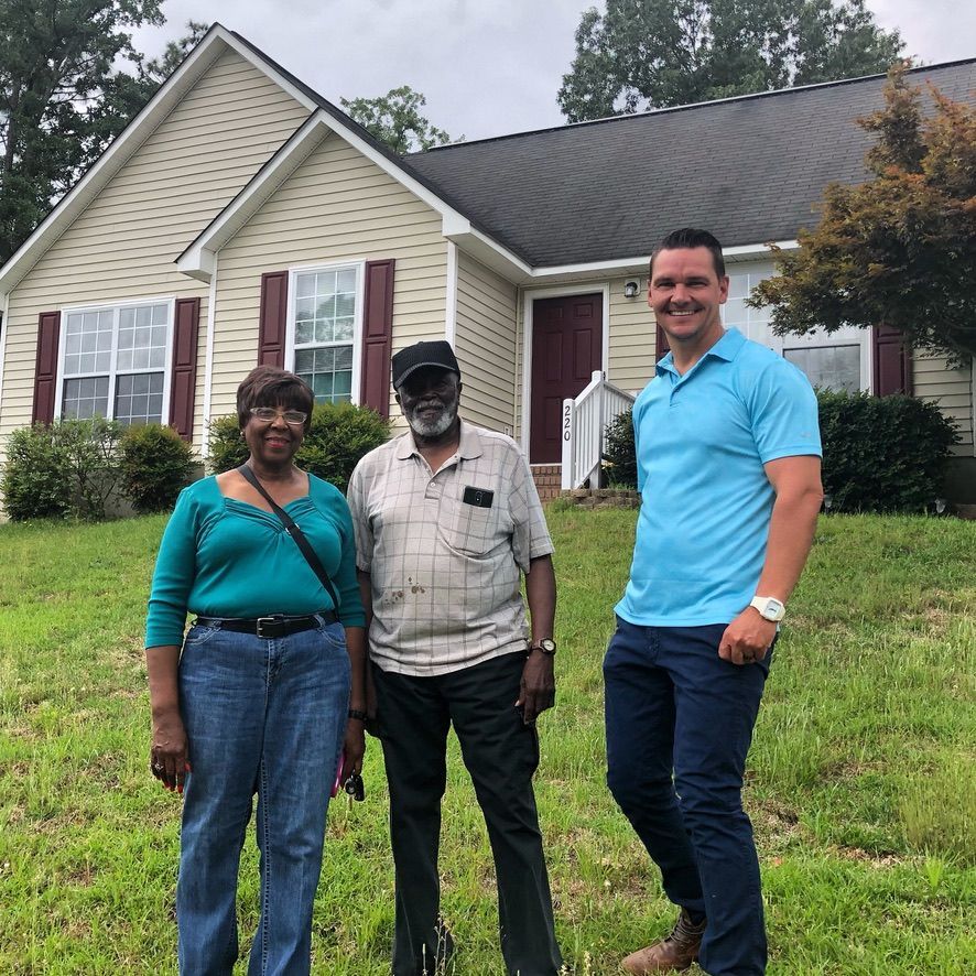 Three people standing on a lawn in front of a house, smiling at the camera.