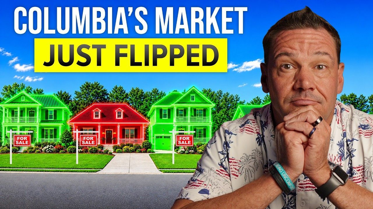A man in a floral shirt poses in front of colorful houses with 'For Sale' signs, discussing the housing market.