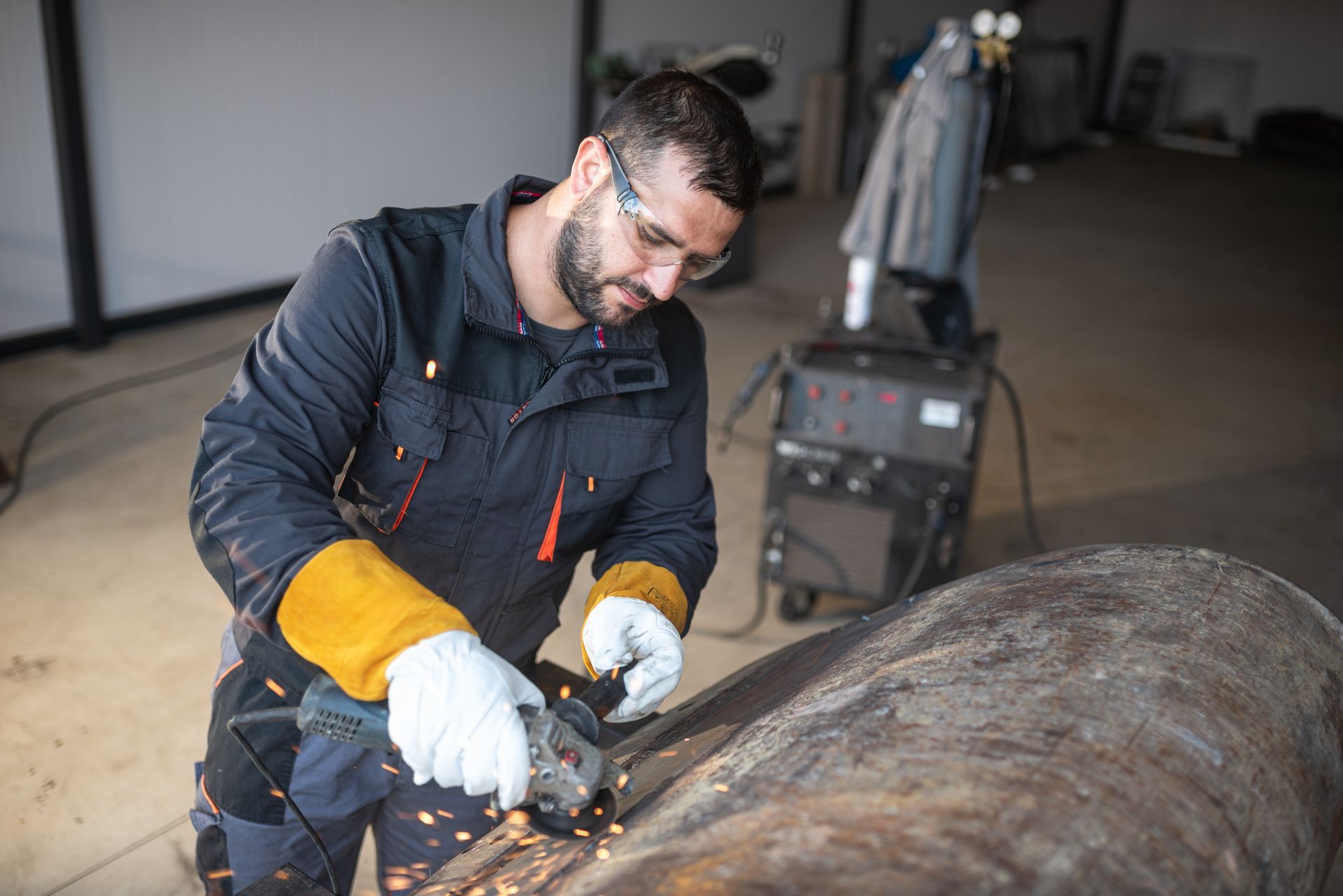 Person wearing safety gear grinds metal pipe in a workshop. Sparks fly. Person wearing safety gear grinds metal pipe in a workshop. Sparks fly.