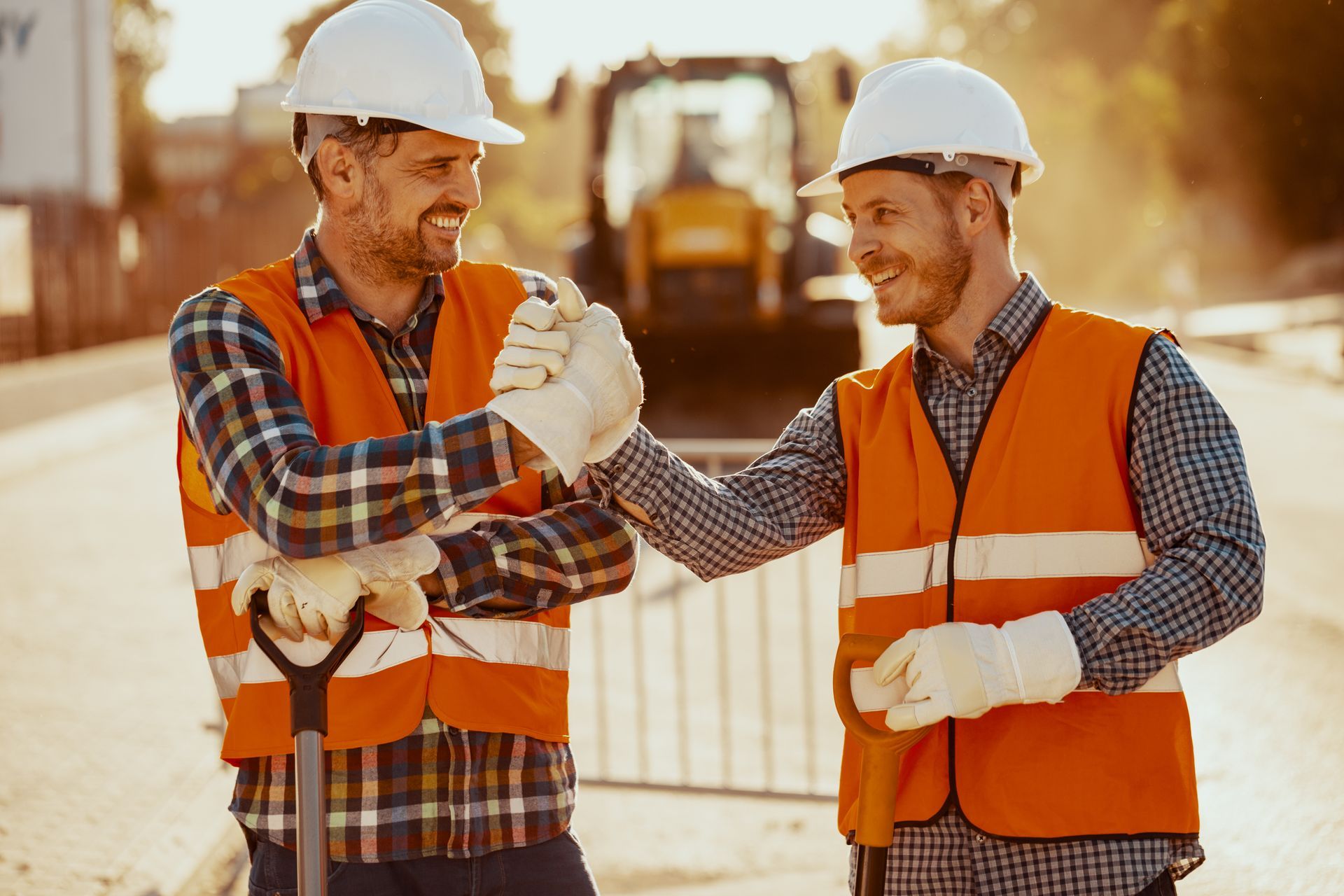 Two people shaking hands over blueprints and hard hats in an office.
