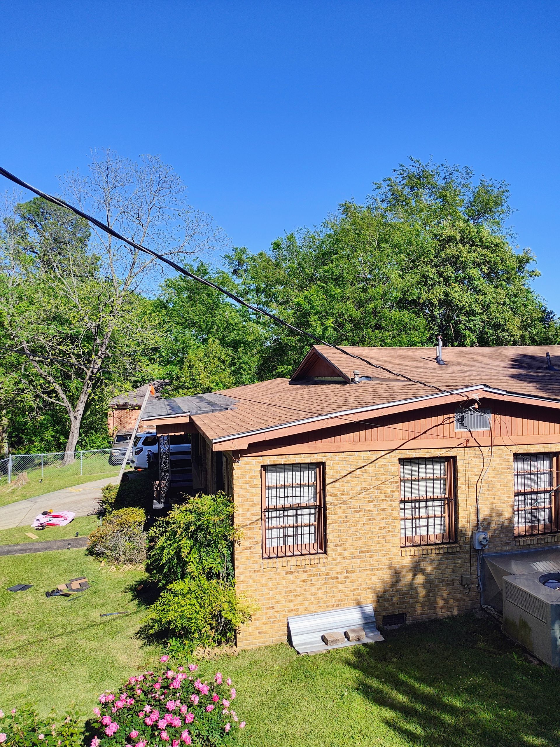 A small brick house with a tile roof is surrounded by trees and grass.