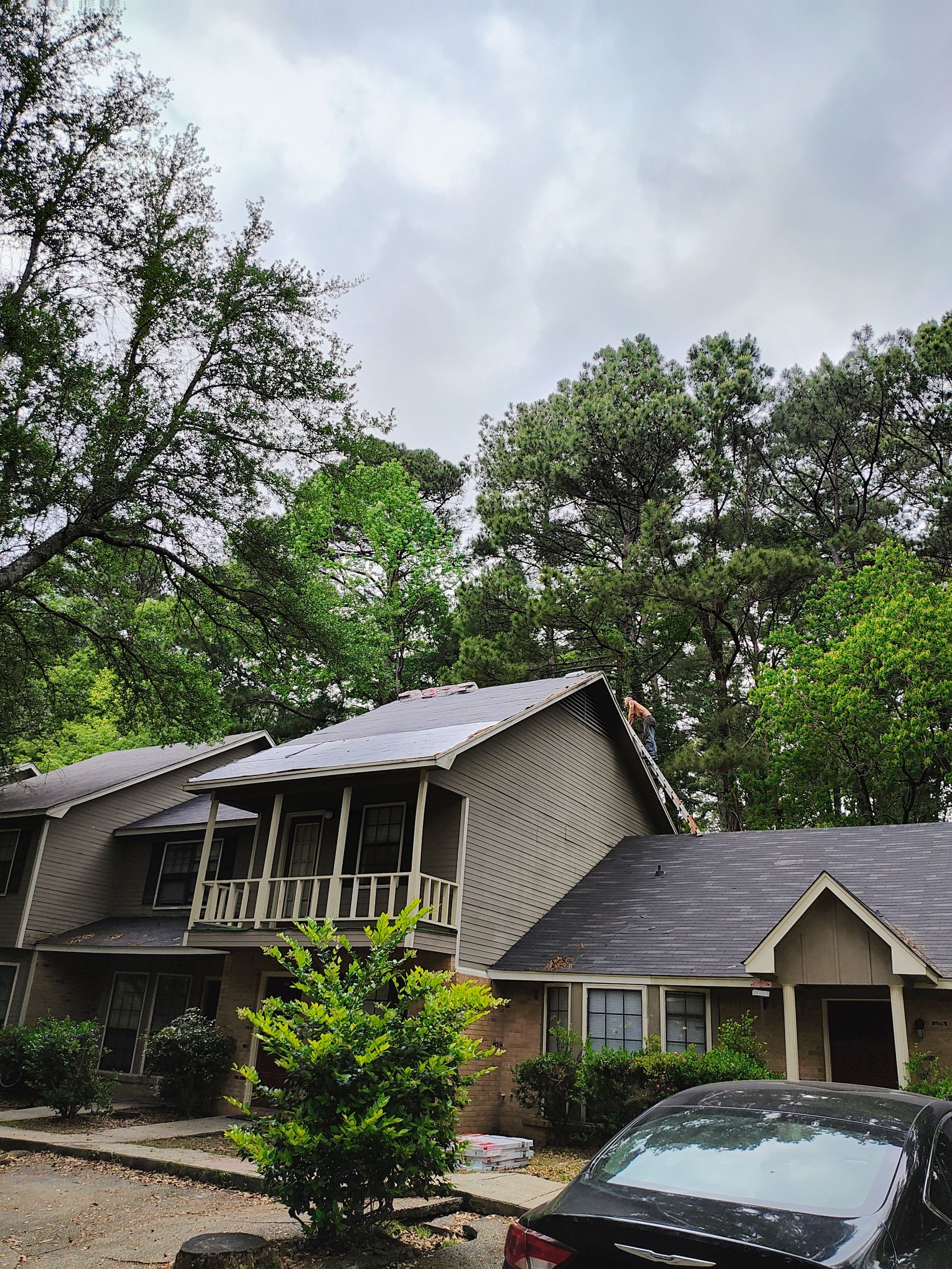 A house with a car parked in front of it and trees in the background.