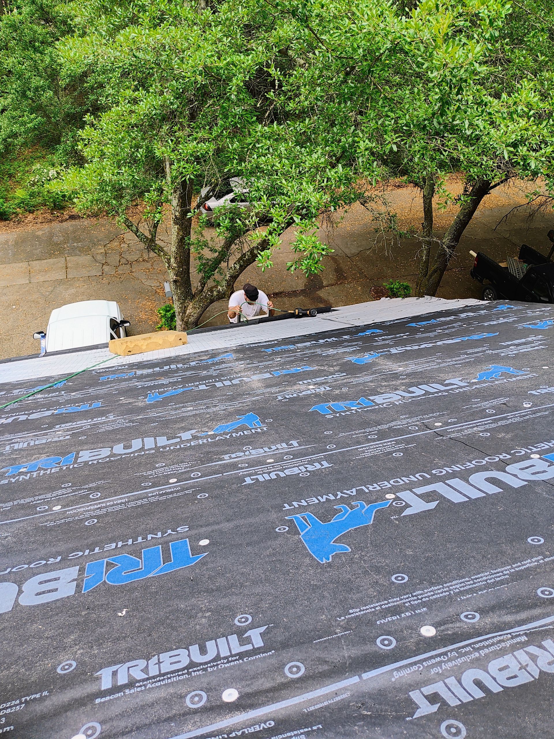 A man is working on a roof with a tree in the background.