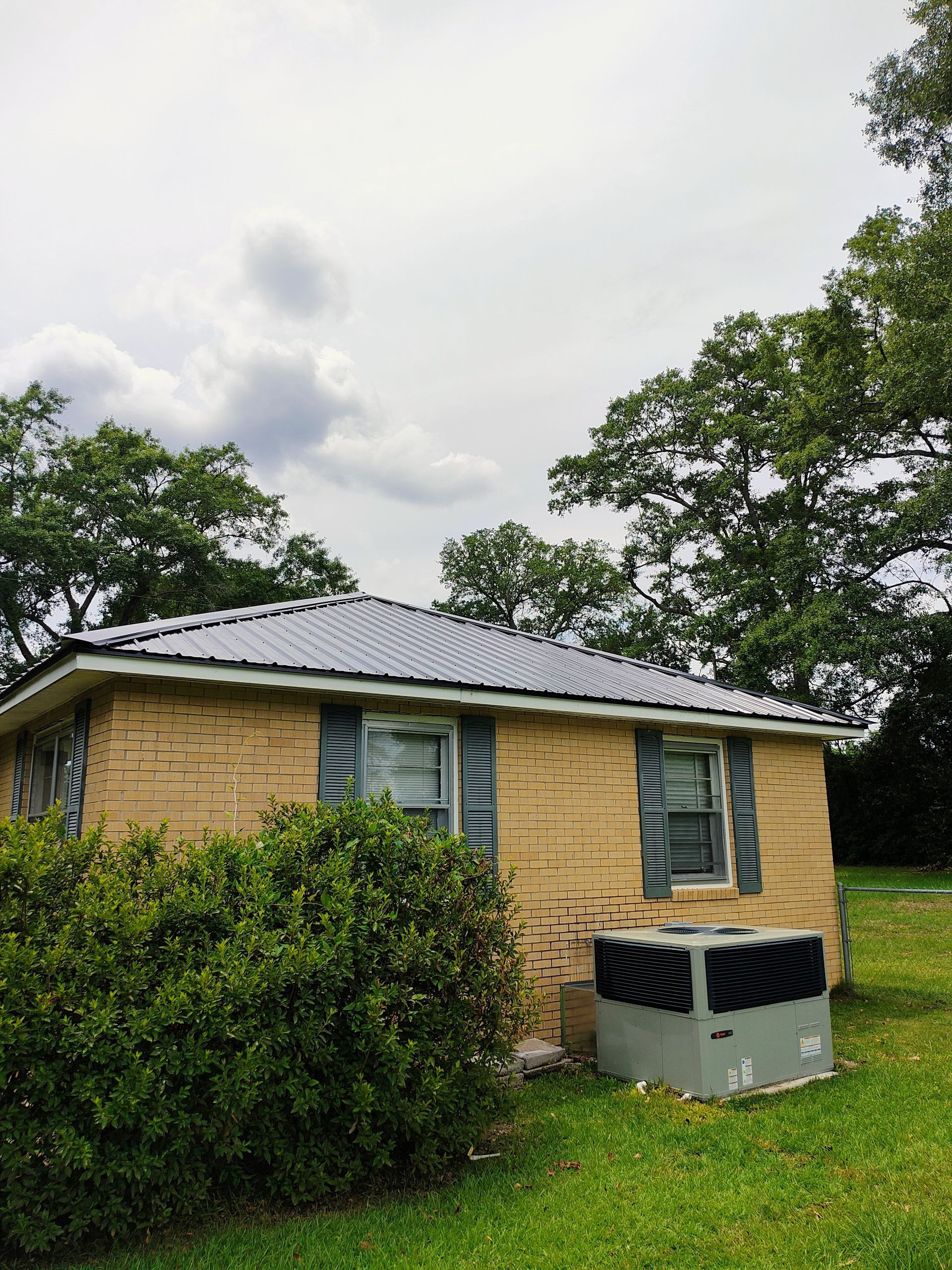 A brick house with a metal roof and an air conditioner in the backyard.