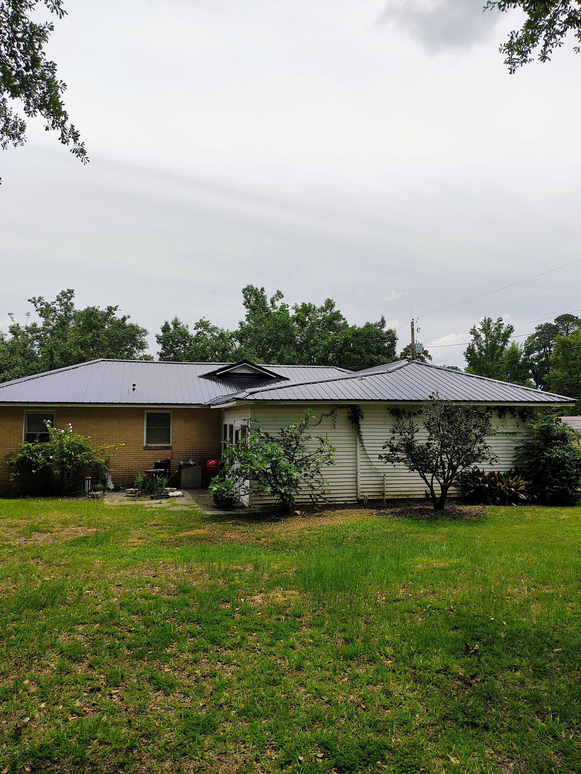 A house with a metal roof is sitting in the middle of a lush green field.