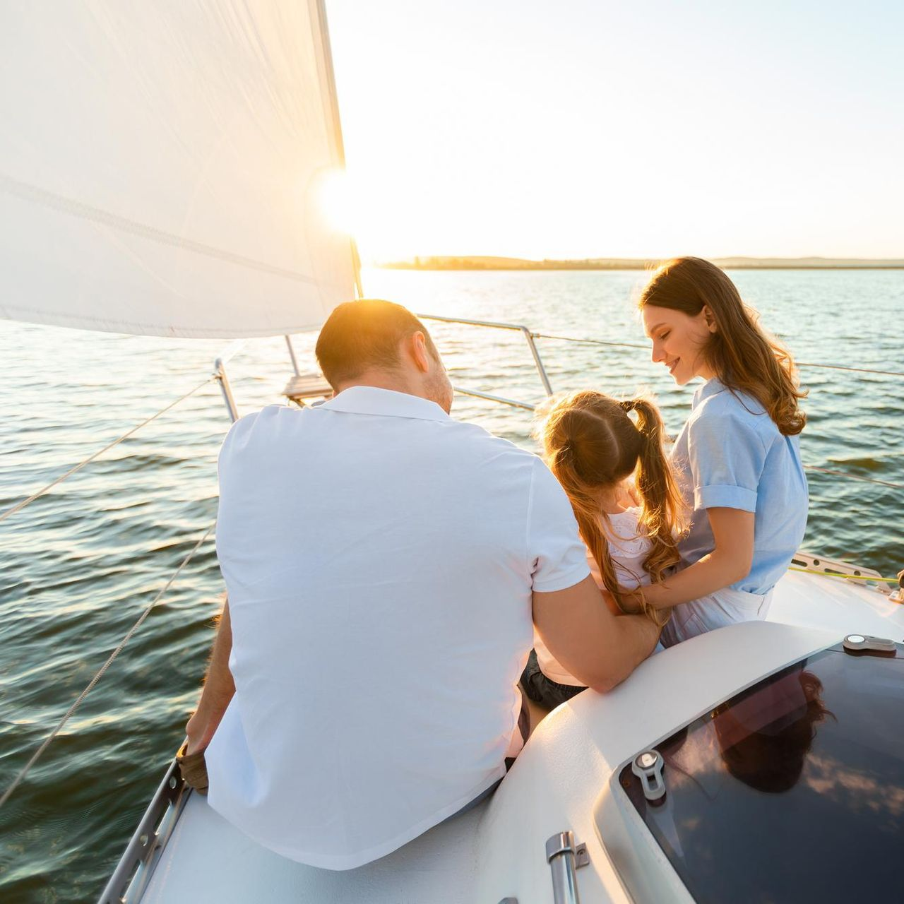 Family sailing on a boat; father facing away, mother and child smiling at the sun.