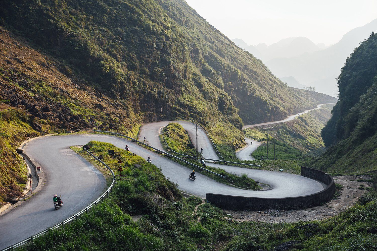 A motorcycle is riding down a winding road in the mountains.