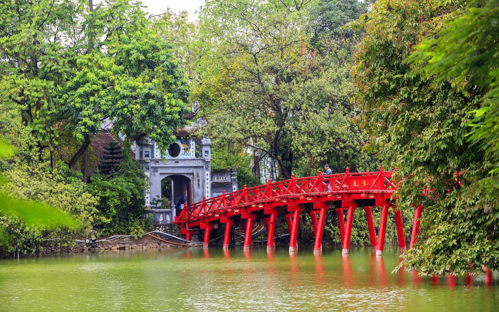 A red bridge over a lake in a park surrounded by trees.