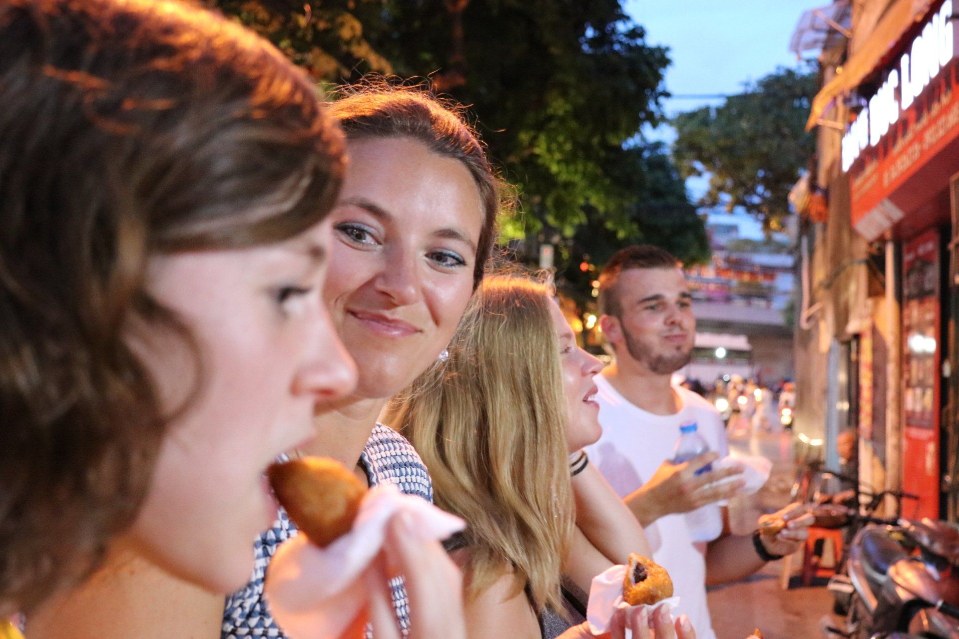 A group of people are standing on a sidewalk eating food.