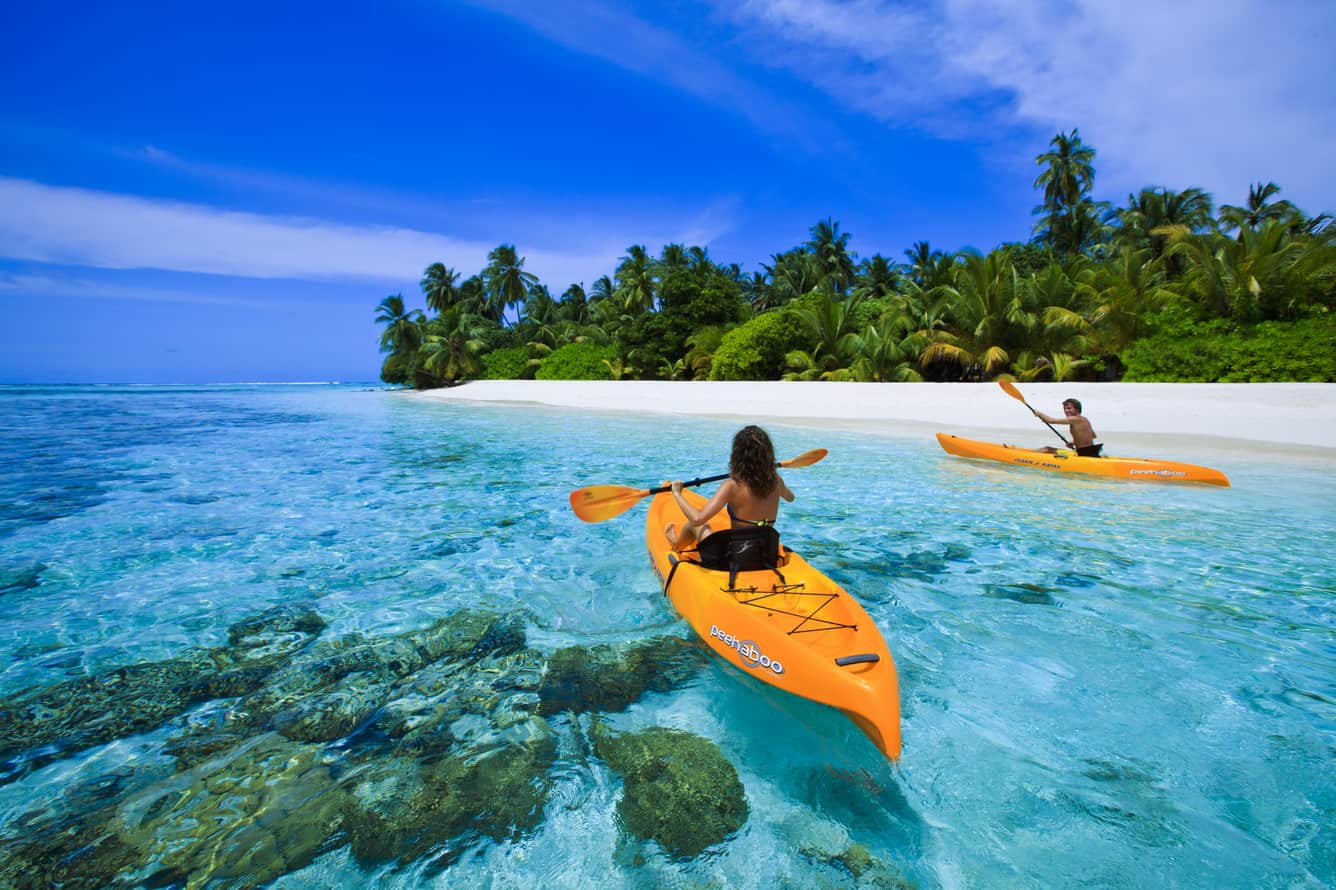 A man and a woman are paddling kayaks in the ocean.