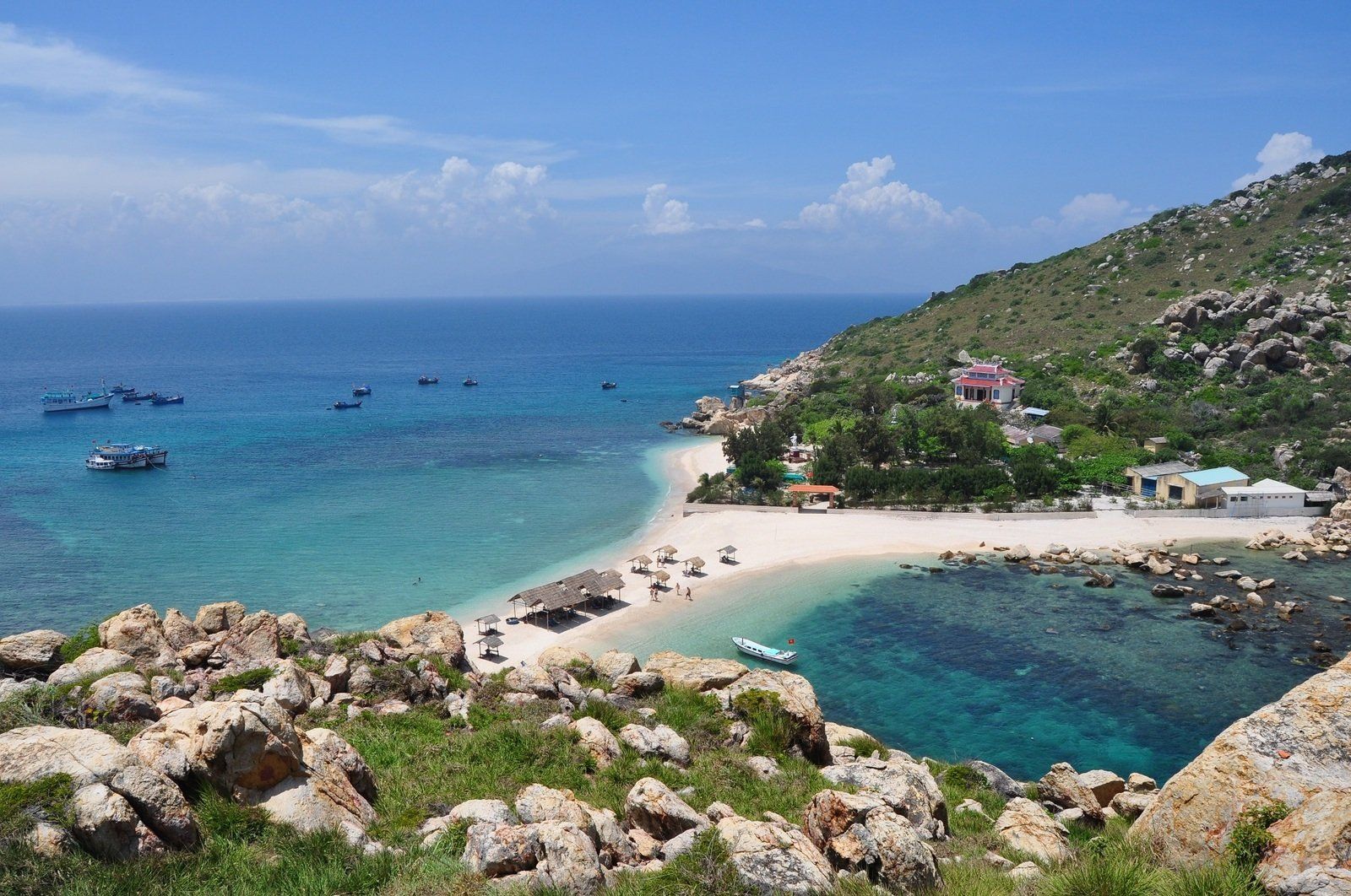 A small island in the middle of the ocean with boats in the water.