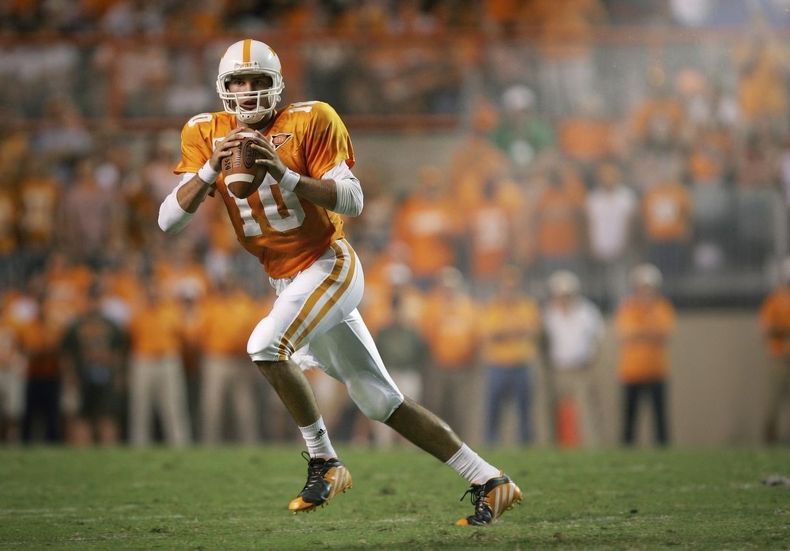 Football player in orange uniform running with the ball on a field, with blurred crowd in the background