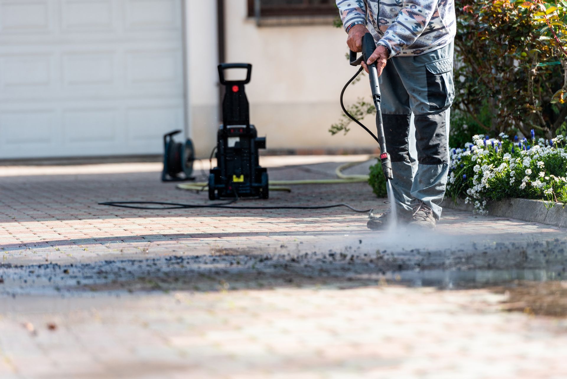 A man is using a high pressure washer to clean a driveway. A man is using a high pressure washer to clean a driveway.