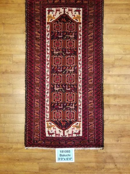 Red and brown Baluchi rug with central geometric design on a wood floor.