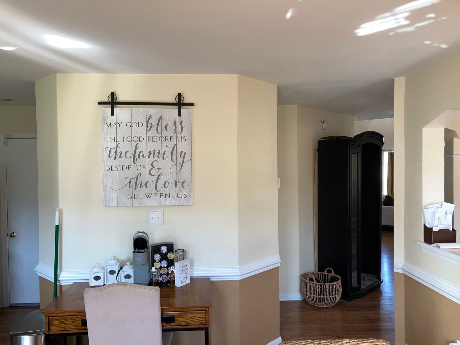Dining nook with a desk, beige walls, white wainscoting, wall art, and a black cabinet in the hall.