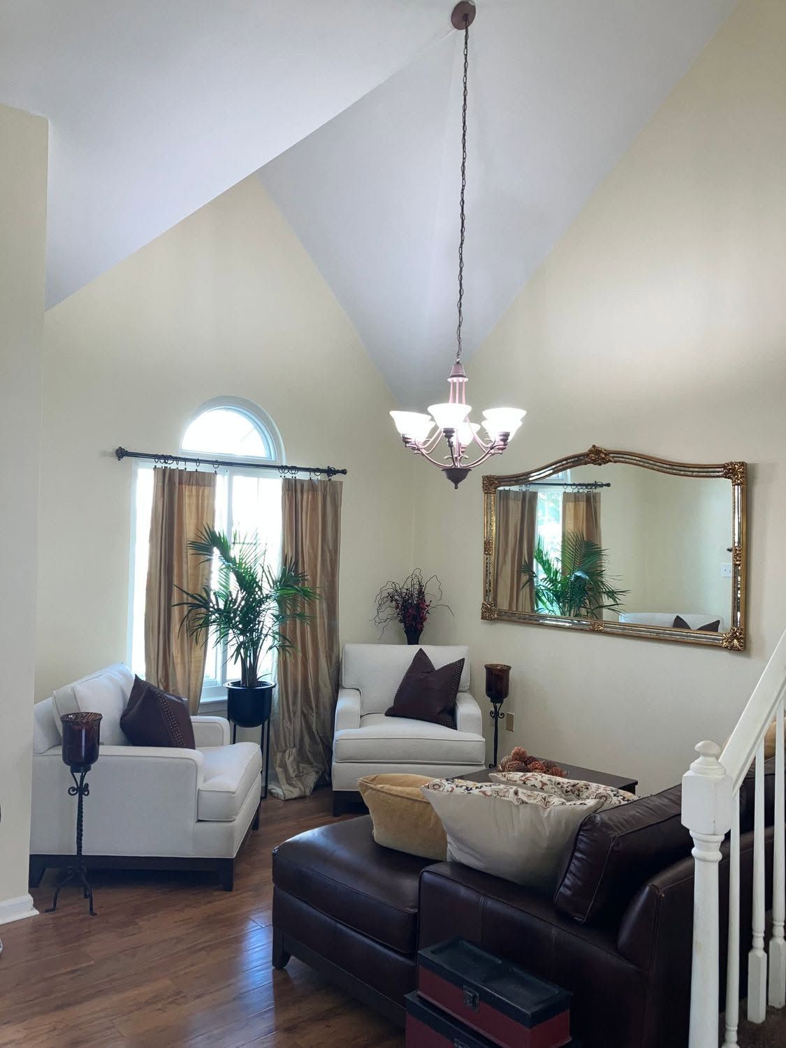 Bright living room with vaulted ceiling, white chairs, dark sofa, chandelier, and large wall mirror.