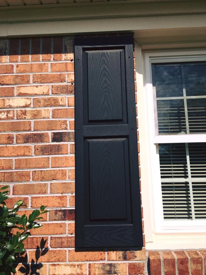 Black shutter on brick house beside a white window with blinds