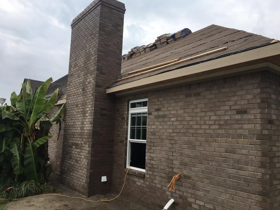 Brick house exterior with chimney and damaged roof shingles after storm