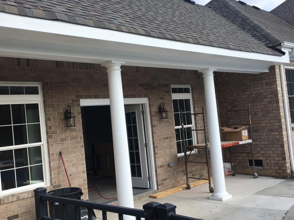 Brick house front porch with white columns, windows, and a dark front door
