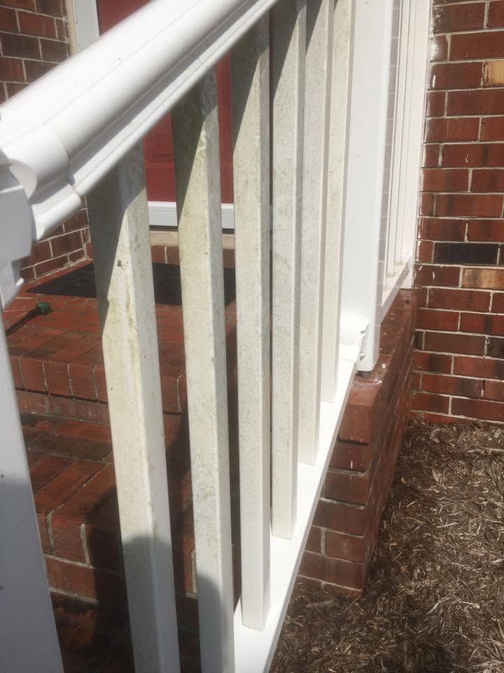 White porch railing beside a brick house with narrow vertical balusters and a sloped handrail