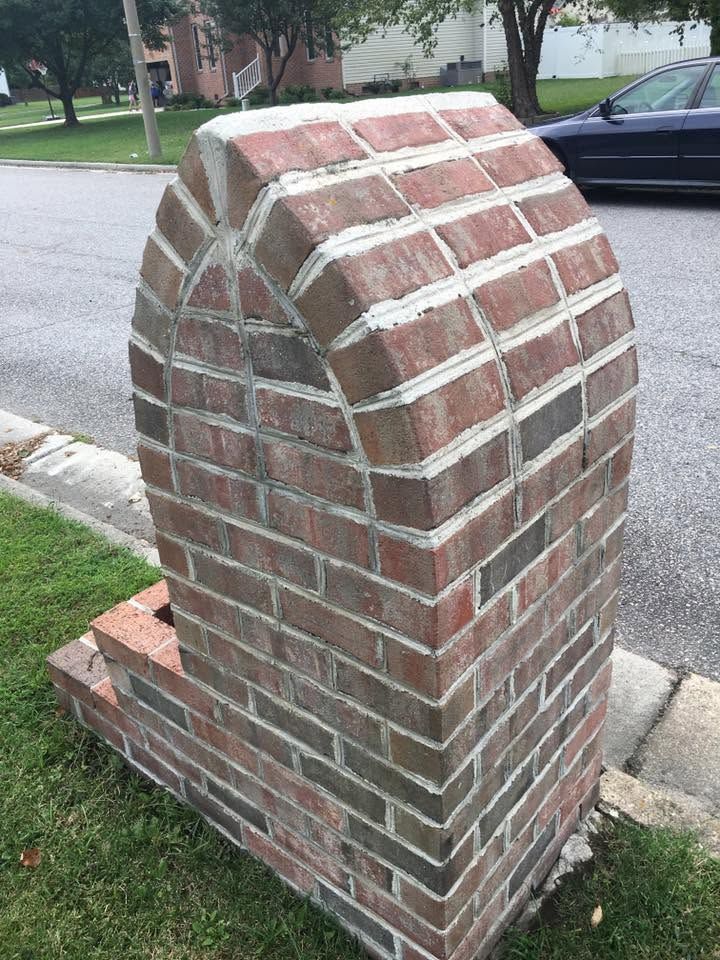 Brick mailbox pillar beside a street, with red-brown bricks and a curved top.