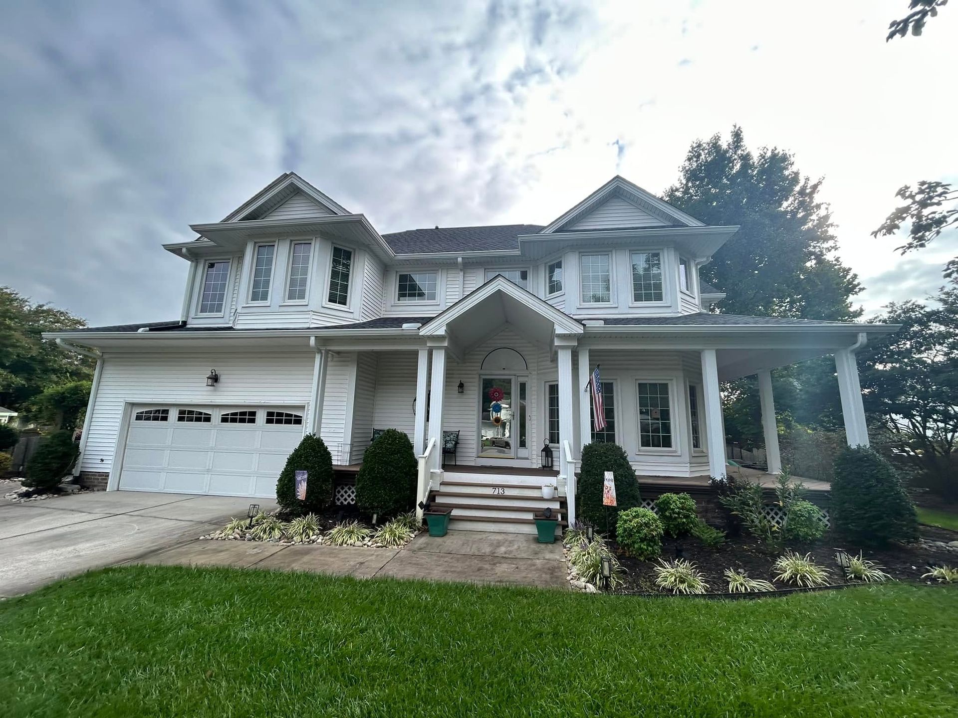 Two-story white house with a front porch, garage, and landscaped yard under a cloudy sky