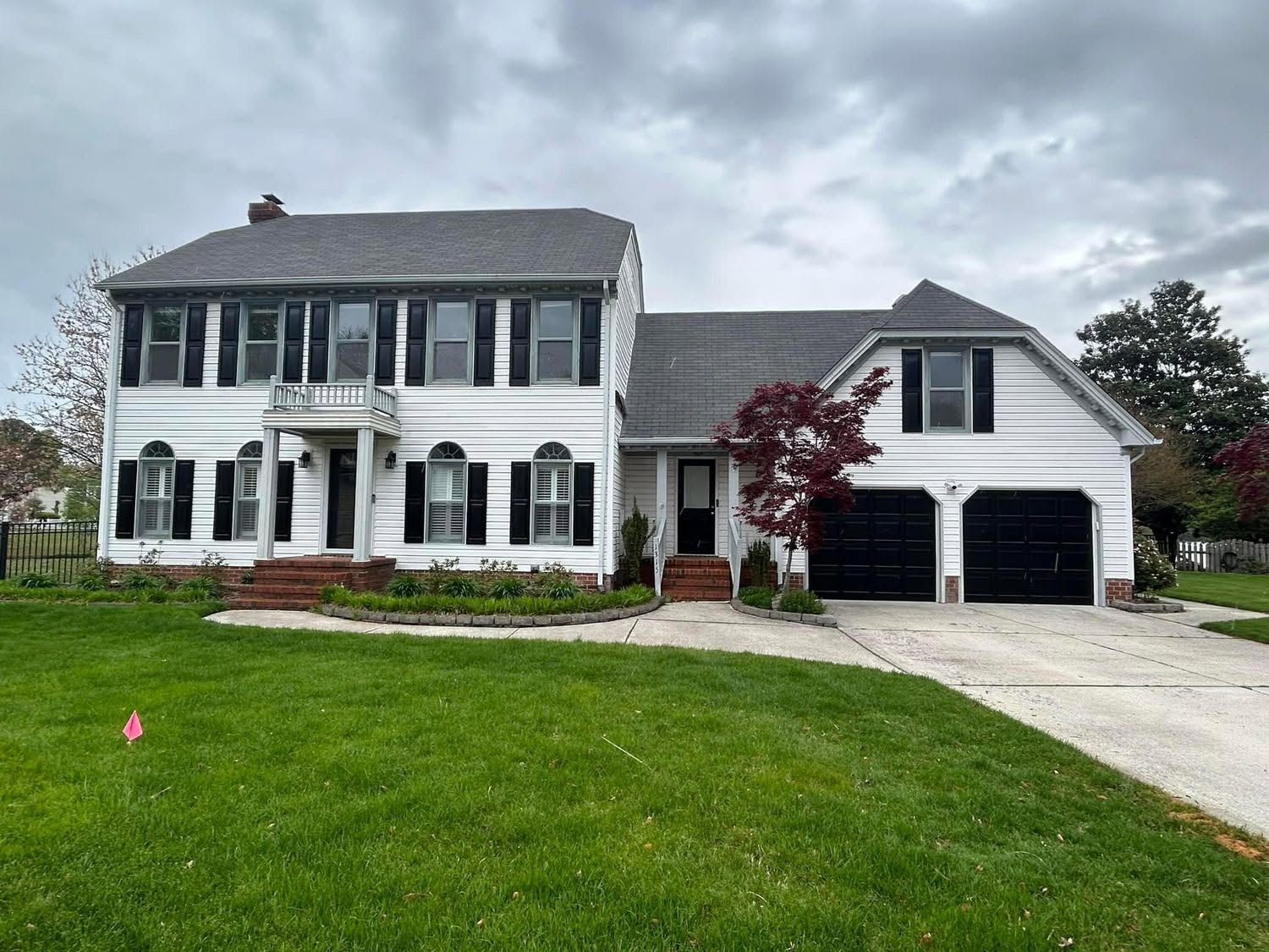 Two-story white house with black shutters, attached garage, and green lawn under cloudy sky