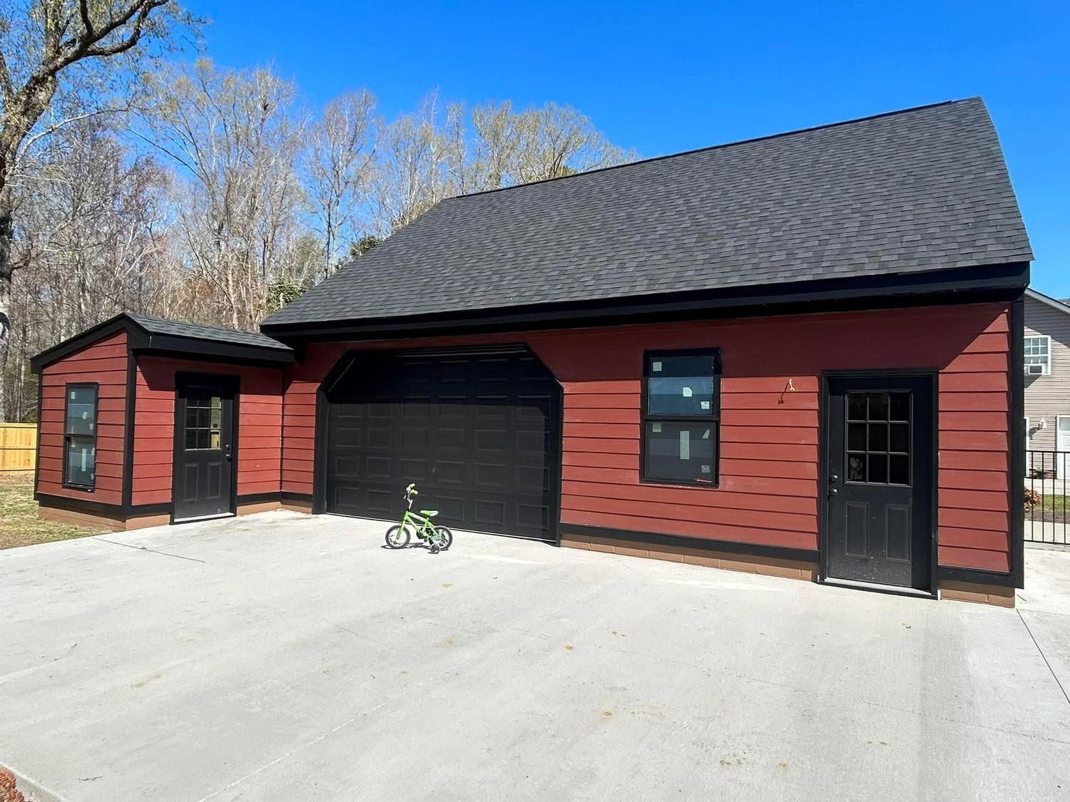 Red barn-style garage with black roof and doors, set on a concrete driveway under a clear sky.