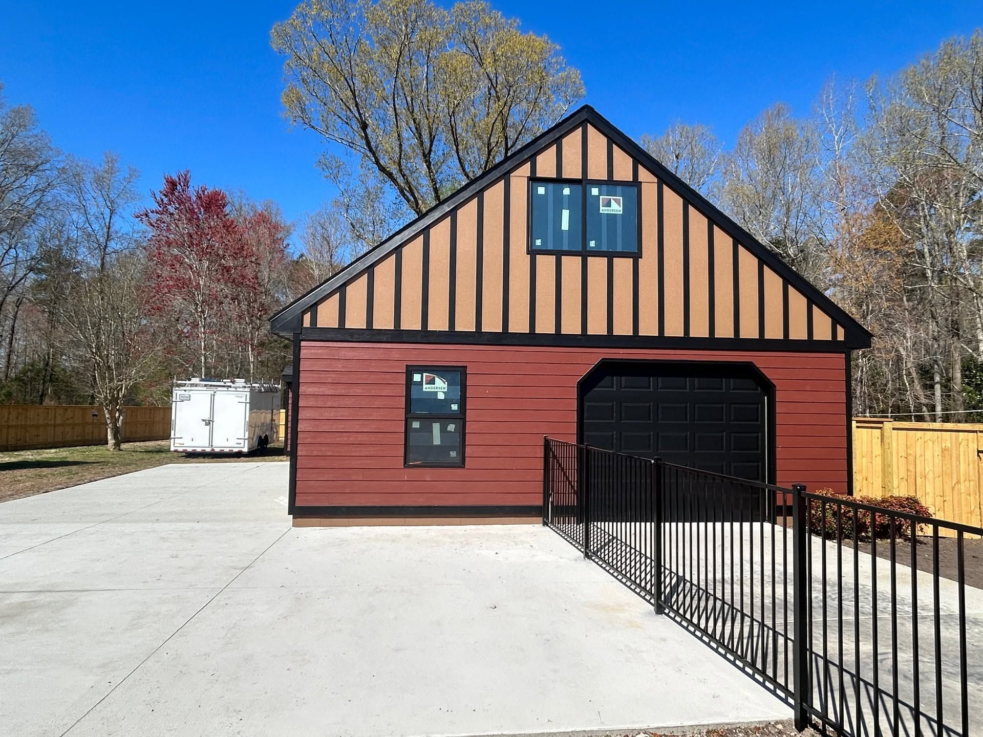 Red barn-style building with black garage door and fenced concrete driveway under a blue sky