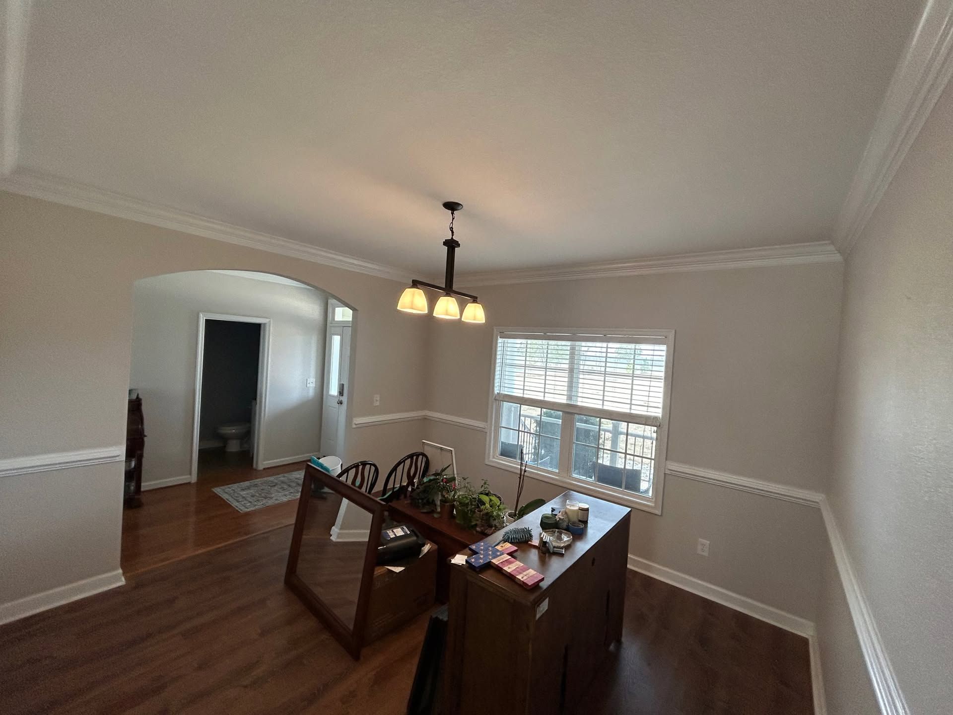 Empty dining room with wood floors, cream walls, chandelier, and bay window.