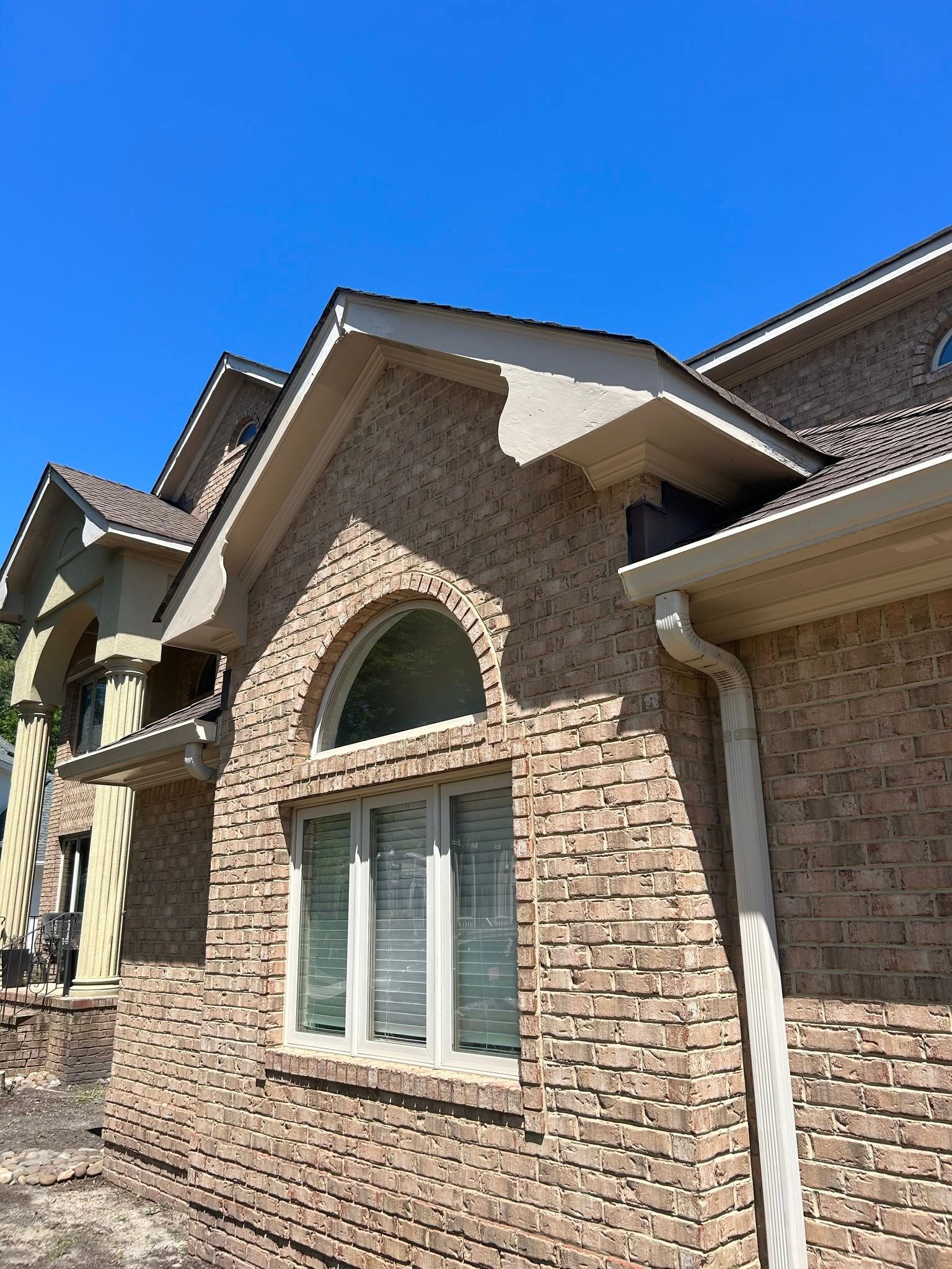 Brick house exterior with arched window and white trim under a clear blue sky