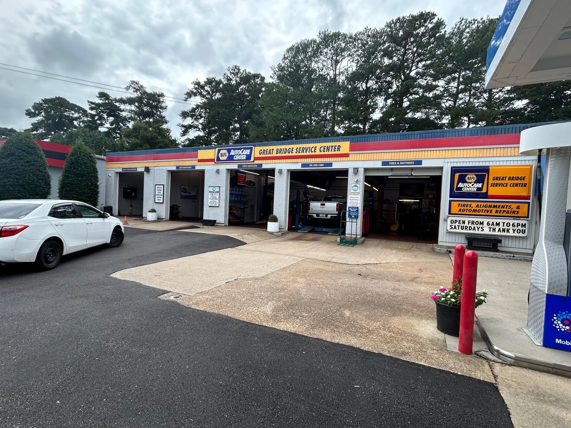Roadside auto service shop with open bays, parked white car, and yellow signage under trees