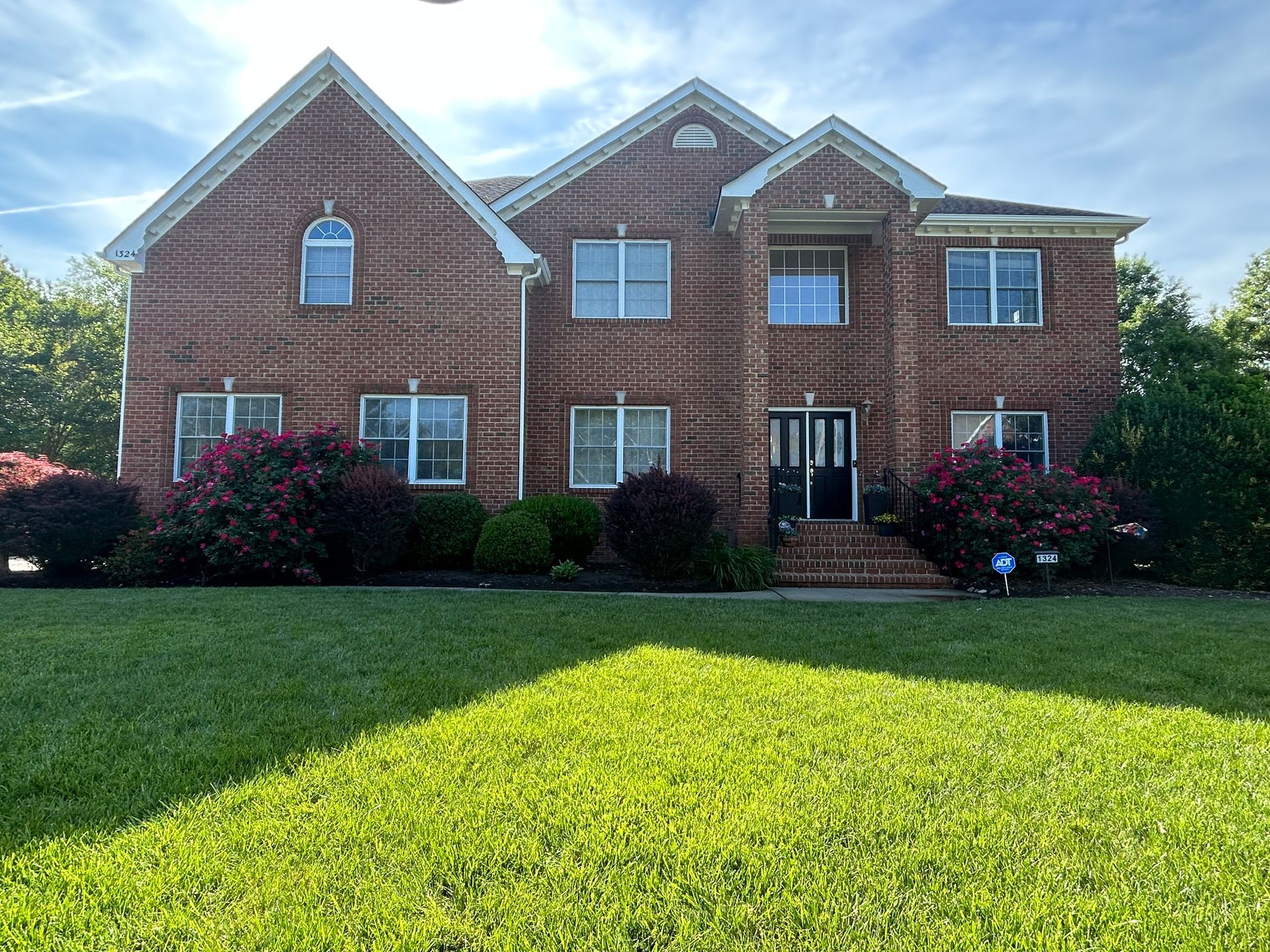 Brick two-story house with white trim and a large green lawn in front.