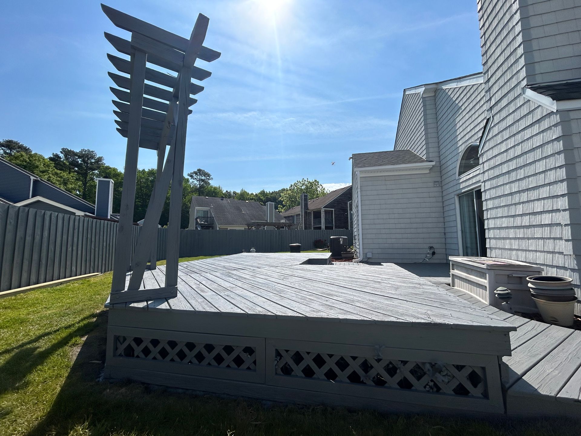 Backyard wooden deck and pergola beside a white house in bright sunlight