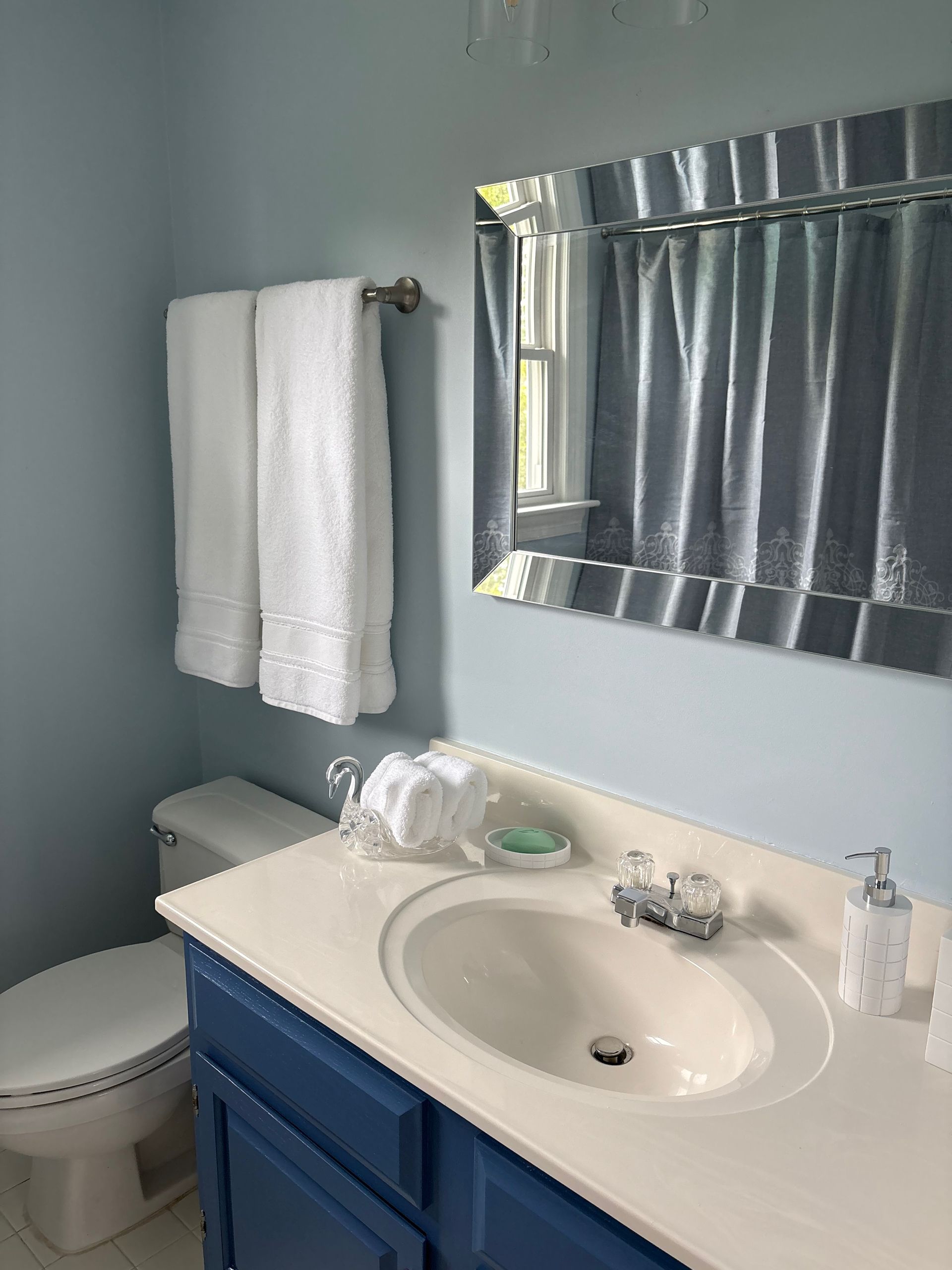 Small bathroom with sink, blue vanity, toilet, towels, and striped window blind