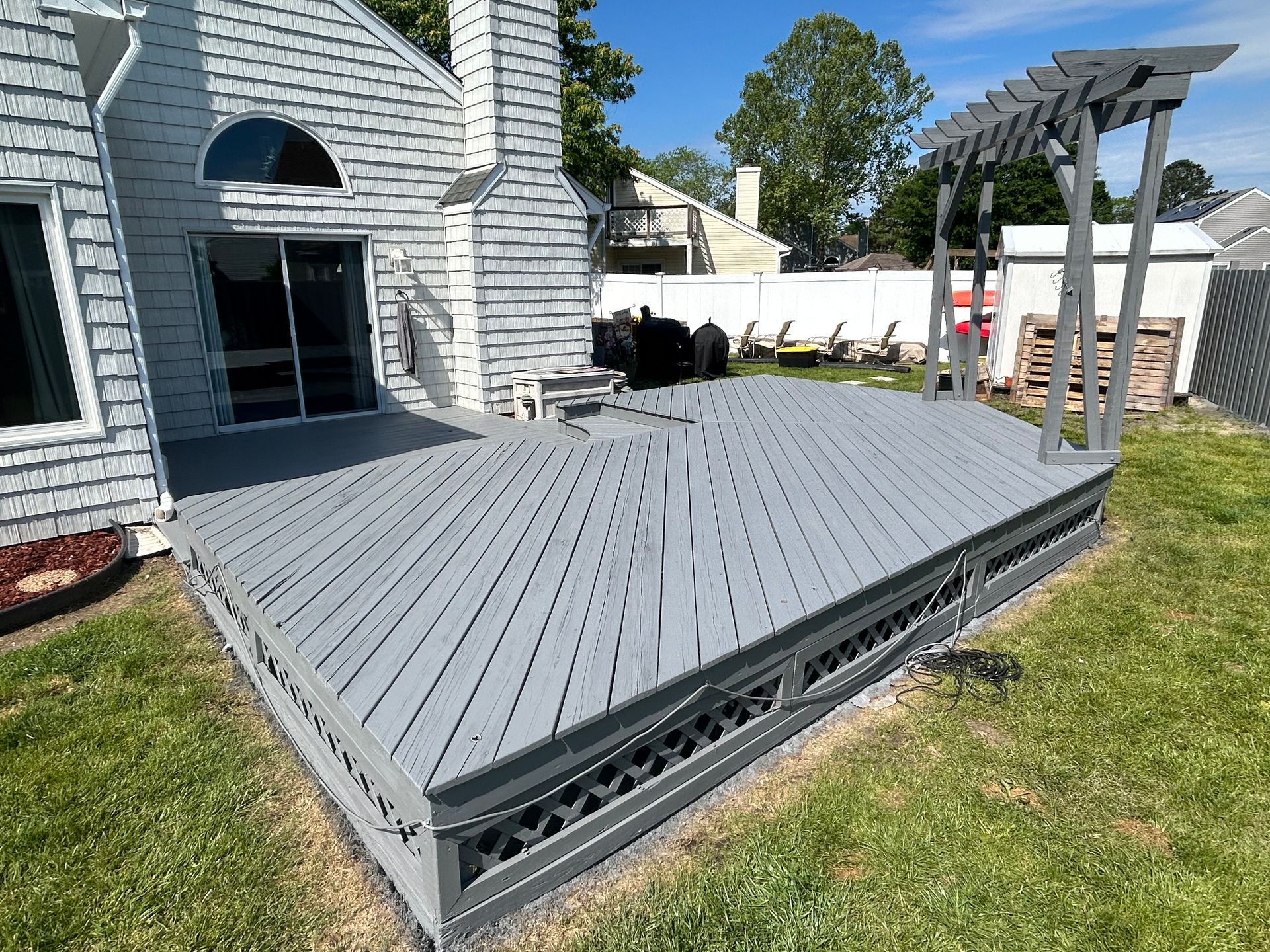Gray backyard deck attached to a house, with pergola posts and black grill nearby.
