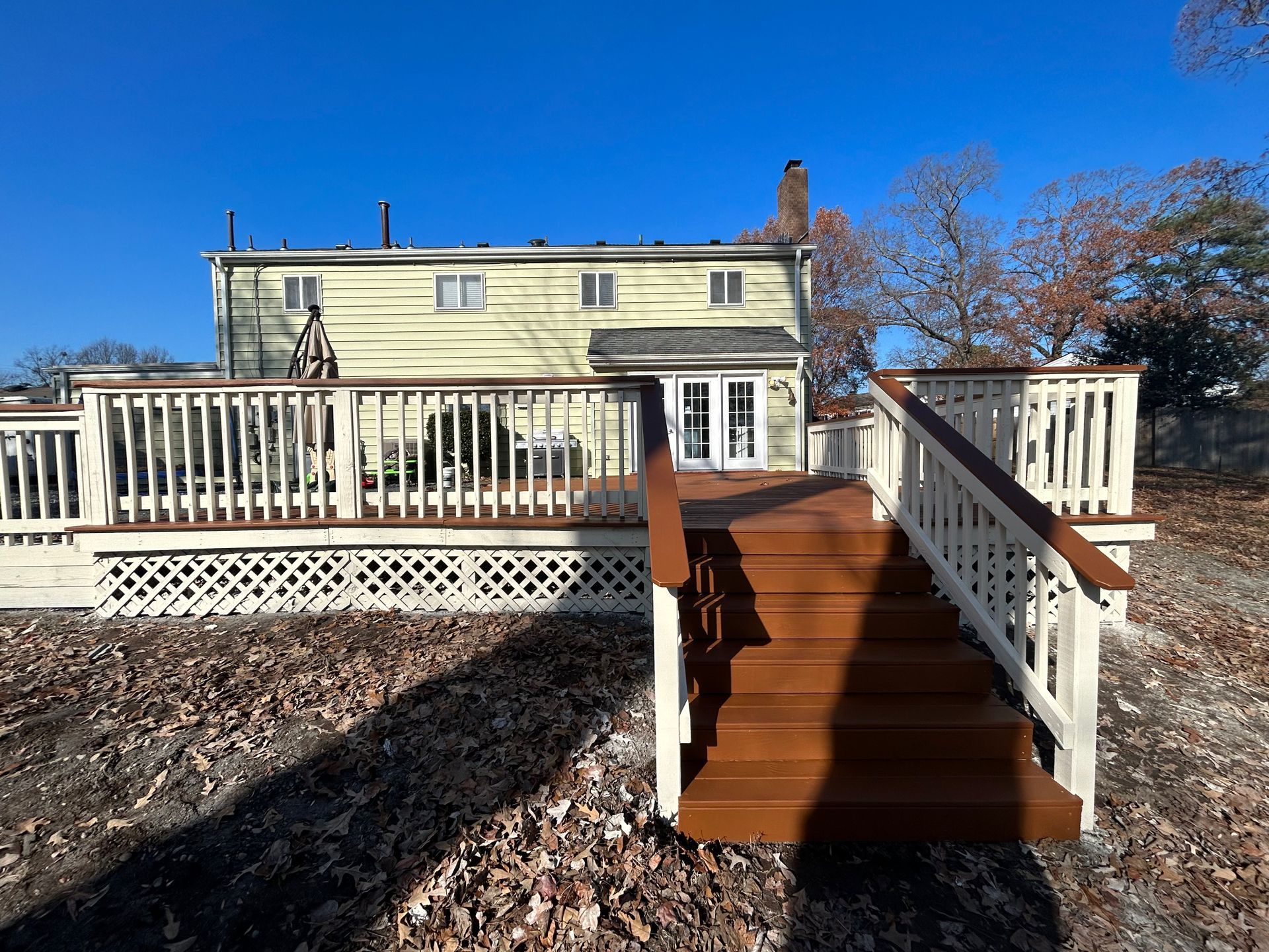Rear deck with wooden steps and white railing leading to a pale yellow house under a clear blue sky