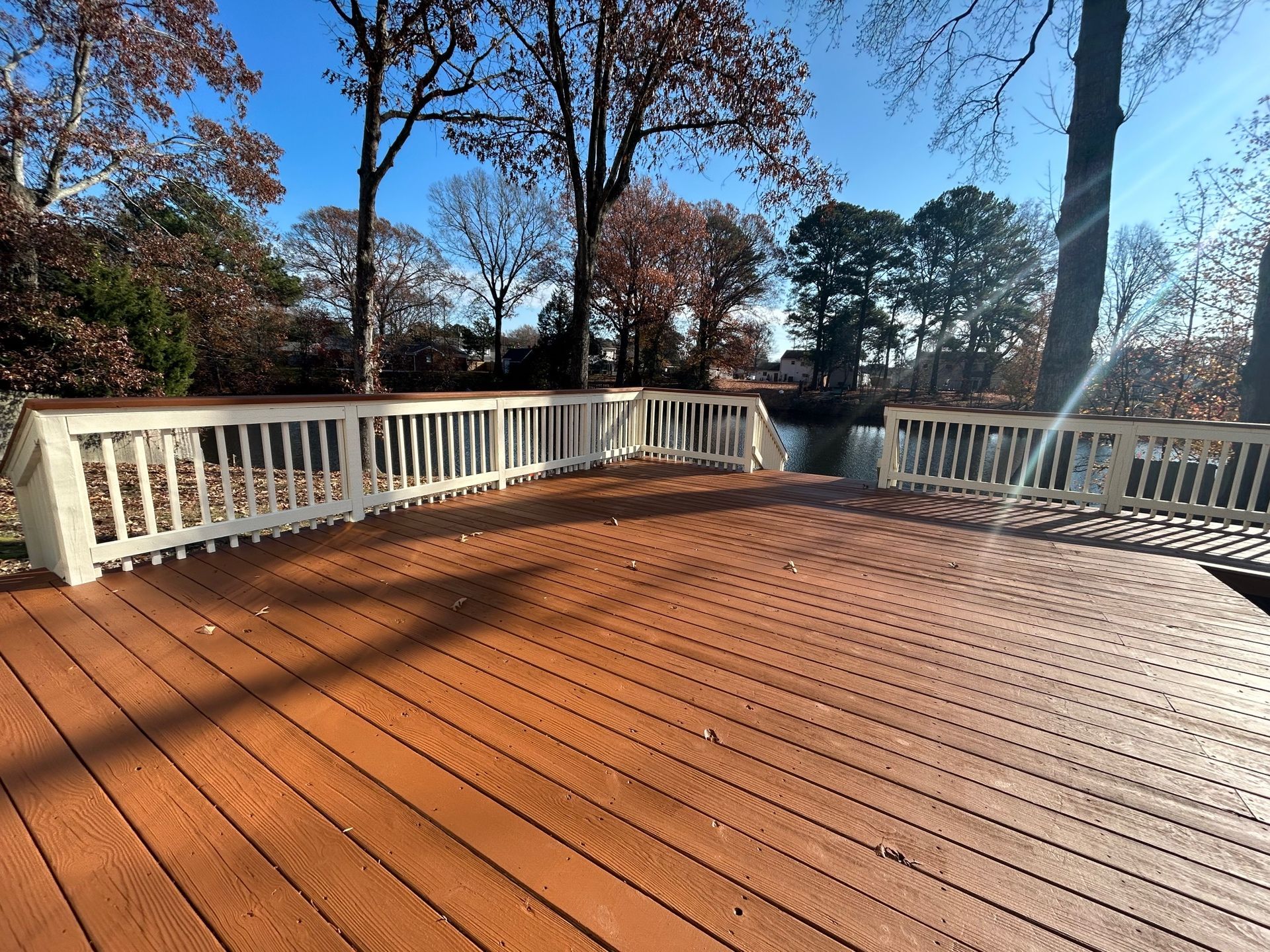 Wooden deck with white railing overlooking leafless trees under a clear blue sky