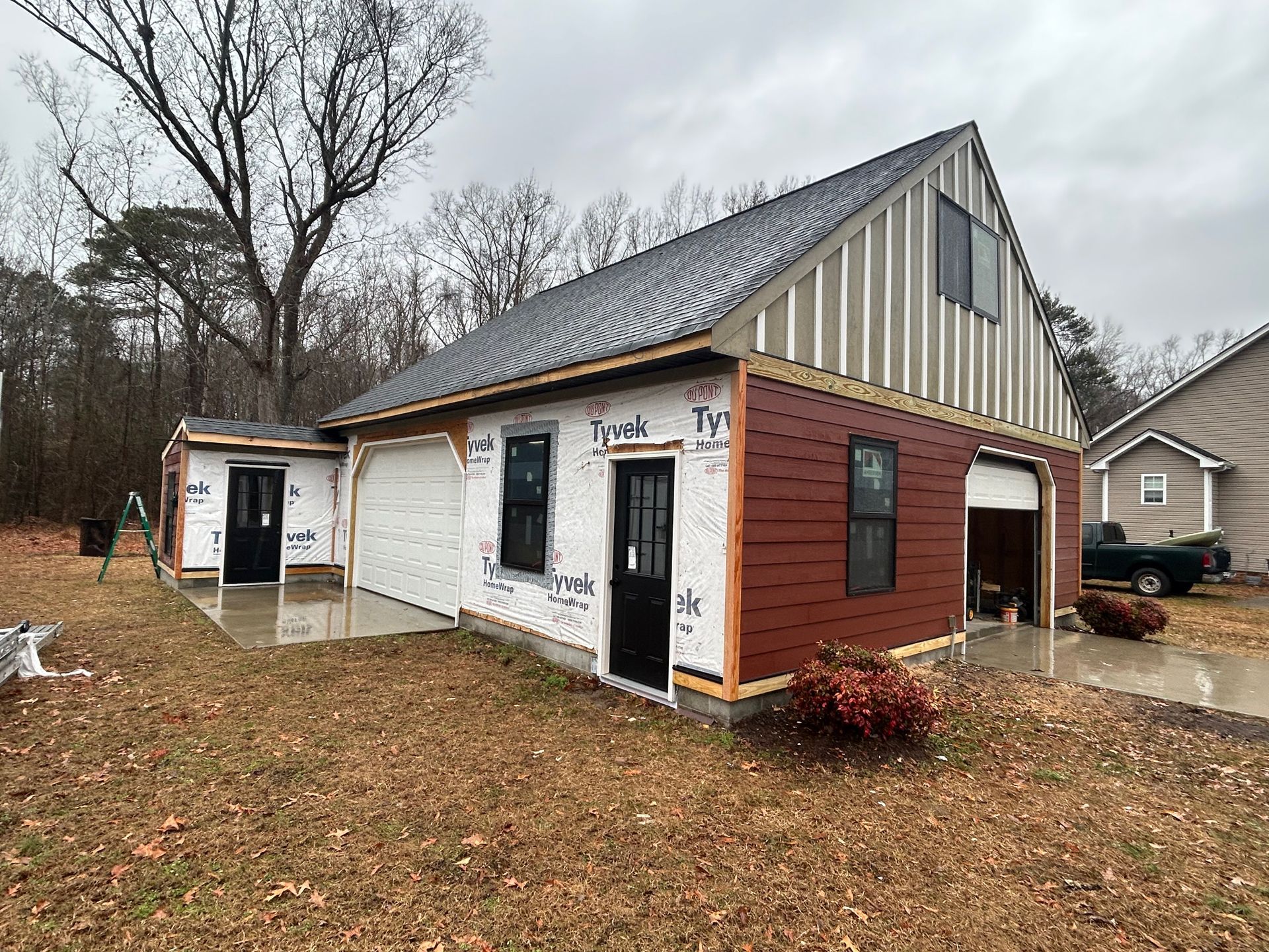 Small unfinished house with white siding, black trim, and an open garage in a leaf-covered yard.