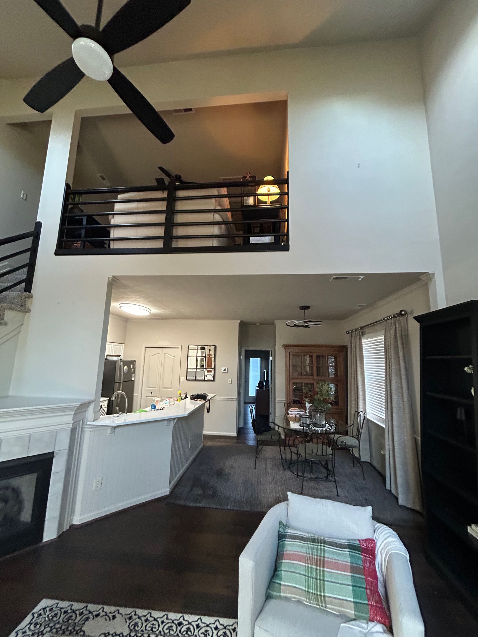Living room with high ceiling, ceiling fan, fireplace, loft railing, and open kitchen.