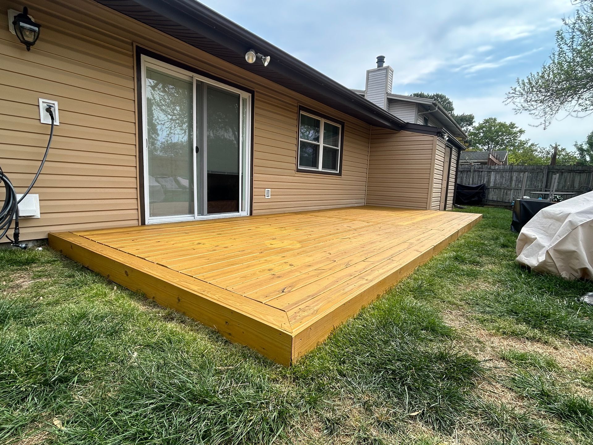 Wooden backyard deck beside a tan house, with sliding glass door and grassy yard.