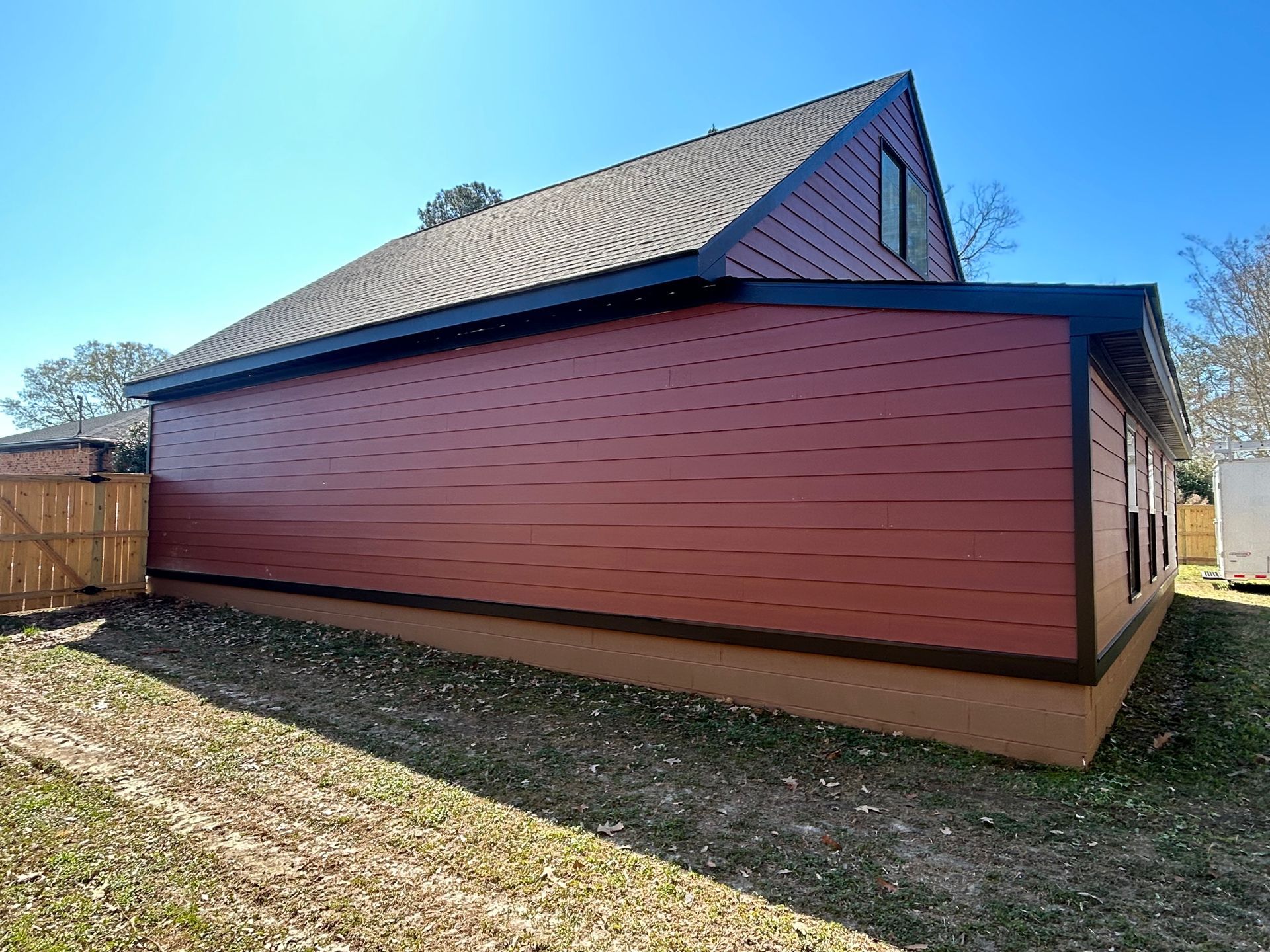Red-sided house with a sloped roof and small gable, viewed from the side in a grassy yard.